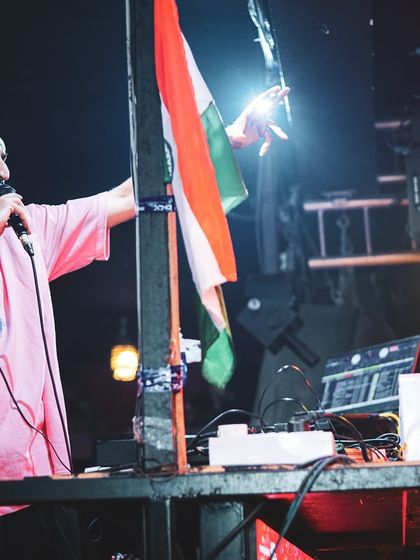 Addressing the crowd on the mic during a Republic Day party, with the tricolor flag proudly displayed.