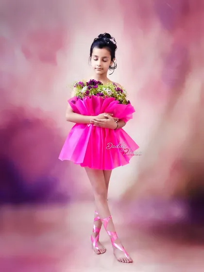 A full length shot showcasing the unique pink floral dress and matching ballet-style ribbons on her feet. The dreamy, cloud like background adds to the magical feel.