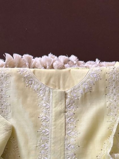 A close-up of the neckline, where the delicate white-on-yellow embroidery is clearly visible.