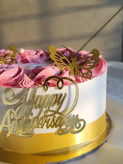A side view of the mango anniversary cake, showing the 'Happy Anniversary' topper and the simple, elegant design.