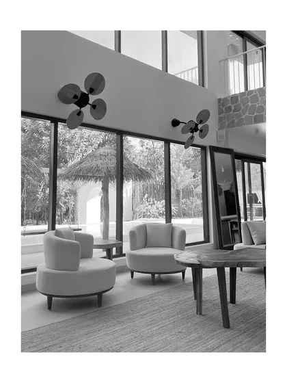 A black and white perspective of the living area, looking out towards the garden. This view highlights the strong vertical lines of the window frames and the unique, petal-like design of the wall-mounted fans.