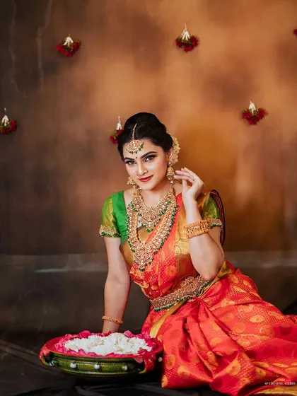 A full-length seated portrait showcasing a stunning red and green bridal saree. The composition includes traditional decorative elements, creating a complete festive scene perfect for a wedding collection lookbook.