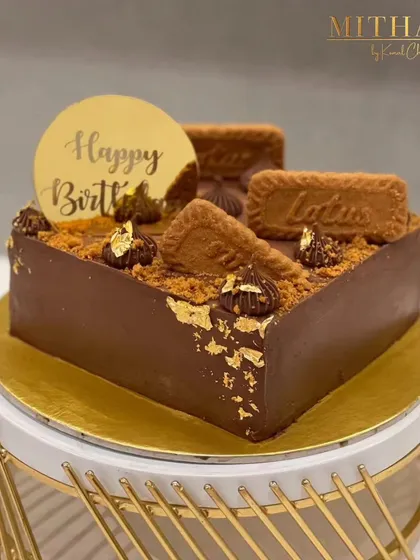 My Lotus Biscoff cake is a divine experience. This square chocolate cake is generously topped with Biscoff biscuits, Biscoff crumble, and dollops of rich frosting, all accented with edible gold leaf for a touch of luxury.