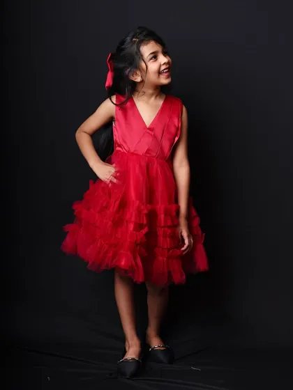 A simple and striking portrait of a young girl in a red party dress against a classic black backdrop. Her upward gaze adds a touch of wonder.
