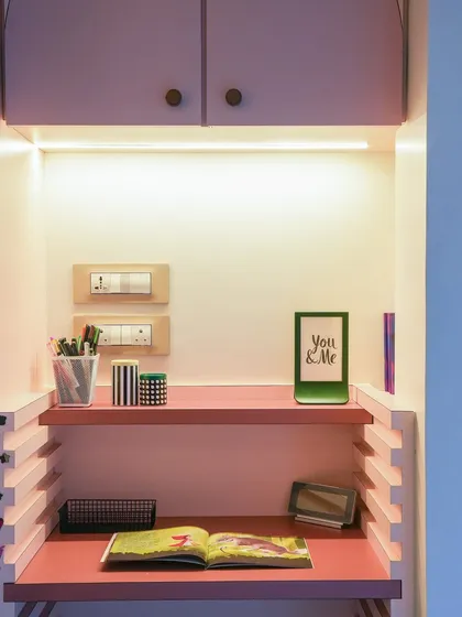 A compact and colorful study nook built into an alcove. The pink desk and shelving create a fun and cheerful workspace, with integrated lighting to keep it bright.