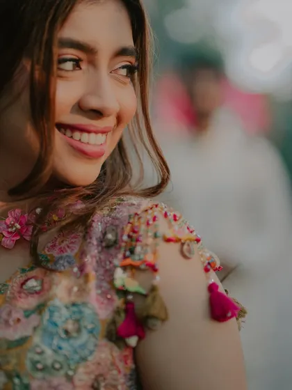 A beautiful close-up of the bride, with the groom softly blurred in the background. This shot highlights her radiant smile and the intricate details of her outfit.