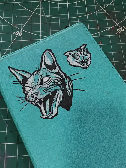 A cool, graphic-style cat illustration painted on a turquoise journal cover.
