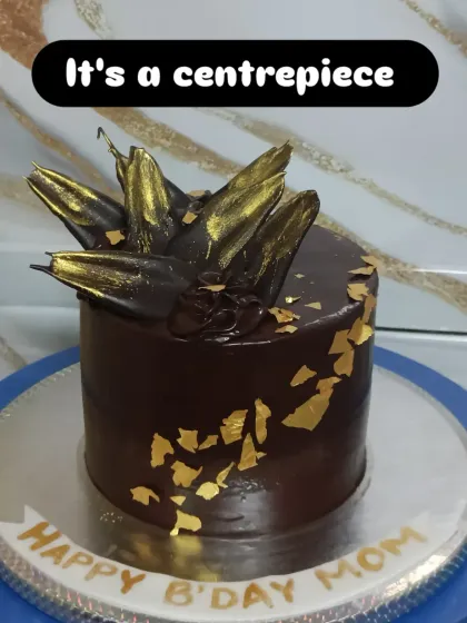 An elegant dark chocolate cake with abstract gold-dusted chocolate shards and edible gold leaf. It's a centerpiece that is both deep and luxurious.