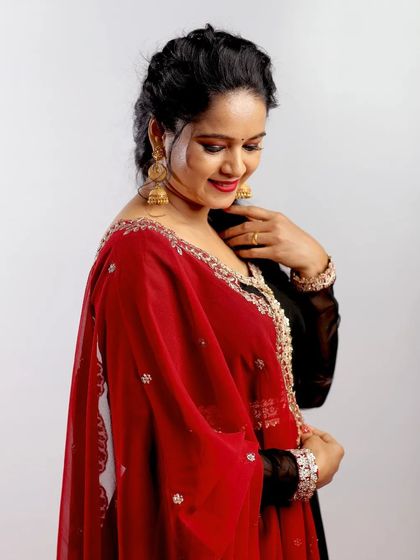 A studio portrait in a black and red Anarkali suit. The clean background and focused lighting draw all attention to the outfit's elegant embroidery and the model's graceful pose.