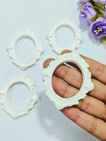 A hand-held view of our white ornate mini frames. The detailed baroque-style design makes them a beautiful choice for crafting unique resin jewelry or small keepsakes.