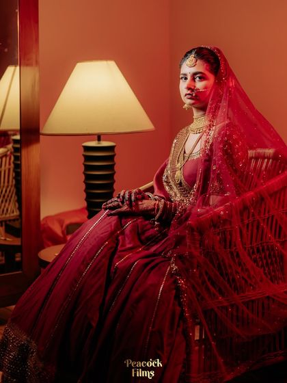 A dramatic bridal portrait, with the bride seated and enveloped in her red veil. The lighting creates a moody and artistic feel.