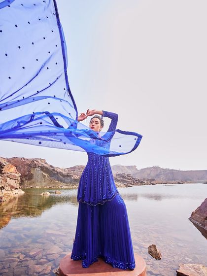 This royal blue sharara set by Nidhika Shekhar is designed to make an impact. The embellished top and pleated pants are paired with a dramatic, flowing dupatta that catches the air beautifully.