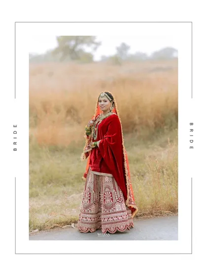 A full-length, artistically framed portrait of the bride in her red lehenga, set against a natural, rustic background.