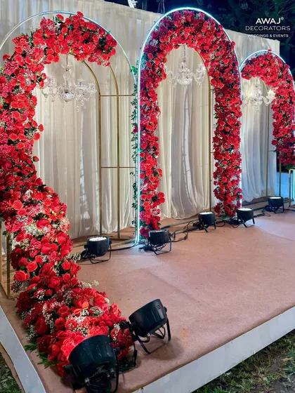 A romantic photo booth with arches of red roses and neon light outlines, set against a simple white curtain.