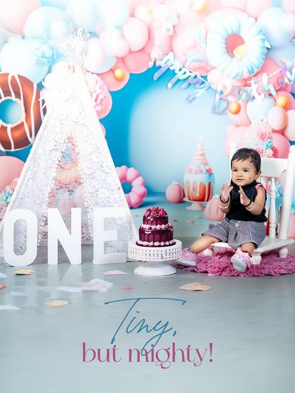 A round of applause for the birthday boy! This shot captures his happy expression as he sits on a little white chair, ready for his cake.