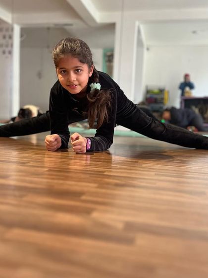 A student in our intermediate class holds a strong center split, looking confidently at the camera. Her posture shows the strength we build alongside flexibility.