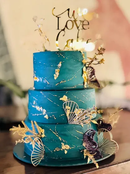 I believe cakes can be modern art. This three-tiered cake features a deep teal buttercream, splattered with gold leaf and accented with elegant fan details. It’s a sophisticated and bold choice for a stylish wedding or anniversary celebration.