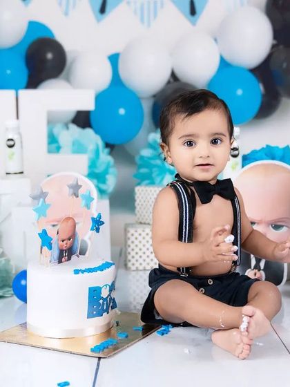 Before the smash! A baby boy sits patiently in his "Boss Baby" setup with his cake, looking dapper in his bow tie and suspenders.