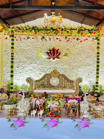 An elegant Seemantham stage with a backdrop made of white flowers. The setup is adorned with a central lotus cutout, traditional dolls, and a beautiful arrangement of offerings.