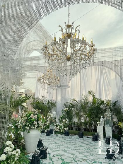 Another angle of the botanical cathedral, showing the interplay of industrial wire mesh structures with classic crystal chandeliers and soft white florals. This design creates a unique contrast that is both modern and timeless.