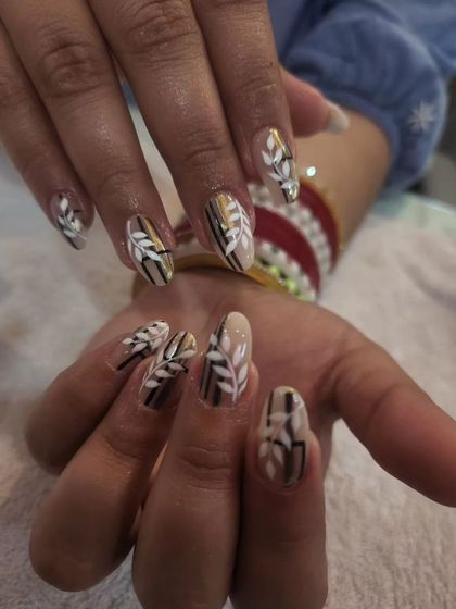 An elegant, hand-painted leaf motif in neutral tones of brown, white, and gold on almond-shaped nails.