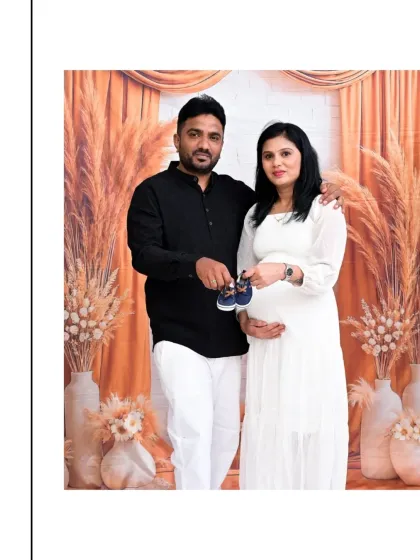 A lovely couple's portrait in our Boho setup. They are holding a pair of baby shoes, a sweet gesture of anticipation. The mix of white and black outfits creates a classic, coordinated look against the earthy backdrop.