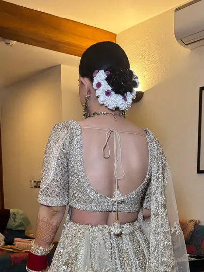 The back of a sleek bridal bun, intricately woven and decorated with a mix of white and purple flowers. This style is perfect for a bride who wants a neat yet detailed look.