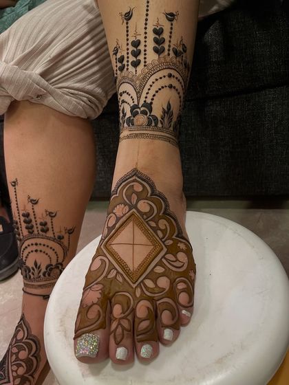 A modern and stylish foot mehandi design. The pattern covers the side of the foot and extends up the leg, like a piece of jewelry.
