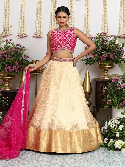 This stunning gold silk lehenga is paired with a vibrant pink Bandhani blouse, creating a beautiful contrast. The embellished belt and sheer dupatta complete this regal look for any grand celebration.