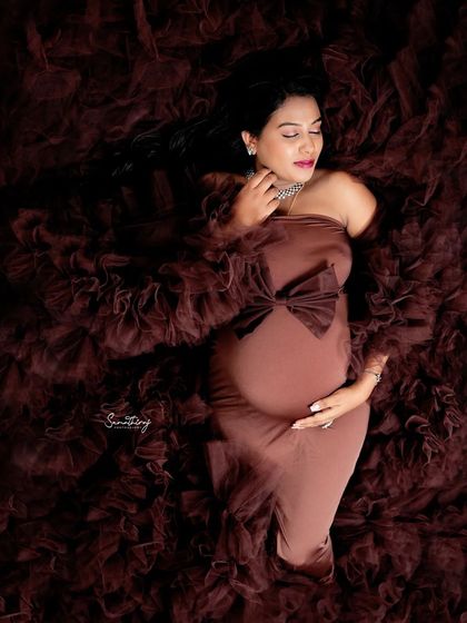 A serene solo portrait of a mother-to-be lying in a bed of brown ruffled fabric. The soft lighting and her peaceful expression create a dreamy and artistic image.