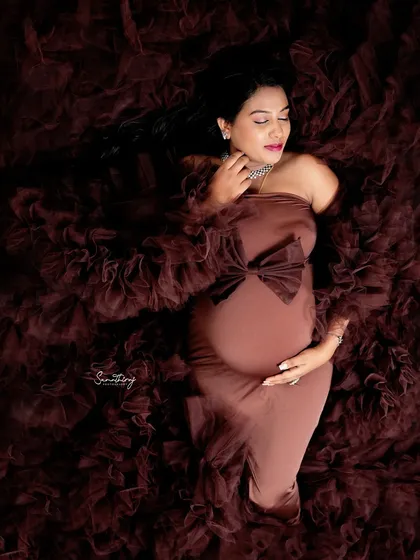 A serene solo portrait of a mother-to-be lying in a bed of brown ruffled fabric. The soft lighting and her peaceful expression create a dreamy and artistic image.