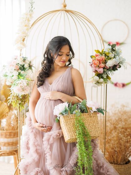 A romantic and whimsical scene, with the mother-to-be surrounded by flowers, a golden birdcage, and a basket of blooms. It's a perfect setup for a fairytale-inspired shoot.