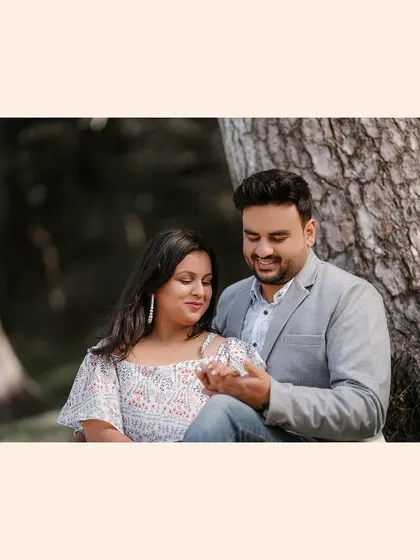 A sweet, casual portrait of a couple sitting together in a forest, capturing a simple, affectionate moment during their pre-wedding session.