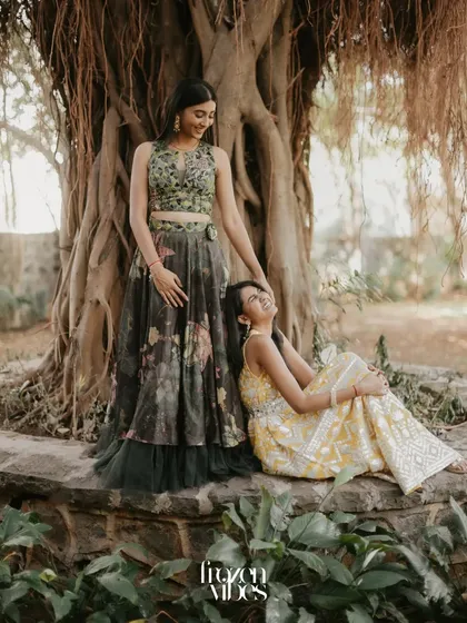 Two sisters share a laugh while sitting together under a large banyan tree. This candid portrait captures a beautiful, natural moment of sibling connection during a family celebration.