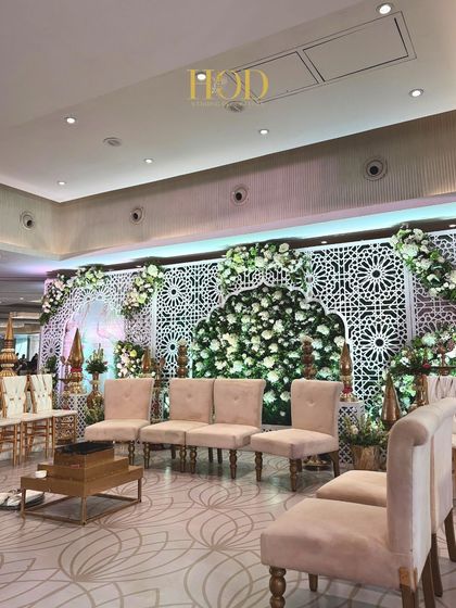 A beautiful Nikah or reception stage featuring white geometric jali panels, with a central arch filled with a dense arrangement of white flowers for a clean and sophisticated look.