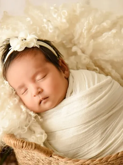 A tight close-up on a sleeping baby's face, swaddled in cream and nestled in a soft, textured basket. These shots capture the delicate features of your newborn.