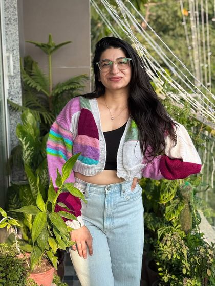 This patchwork cardigan features a unique color combination of purple, pink, and white. It's a one-of-a-kind piece that showcases our love for creative color palettes and cozy, chunky designs.