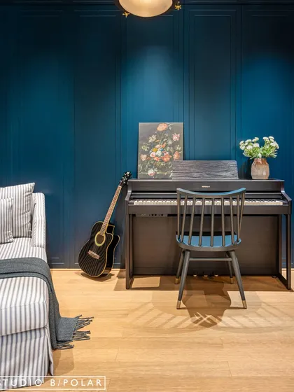 Inside the music room, a piano and guitar are set against the deep blue paneled wall, creating an inspiring space for creativity. The design is cozy, sophisticated, and acoustically private.