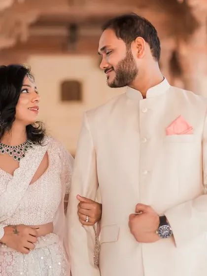 A classic walking shot through a sunlit palace corridor in Jaipur. The couple is linked arm-in-arm, sharing a look of love and admiration, dressed in elegant, complementary outfits.