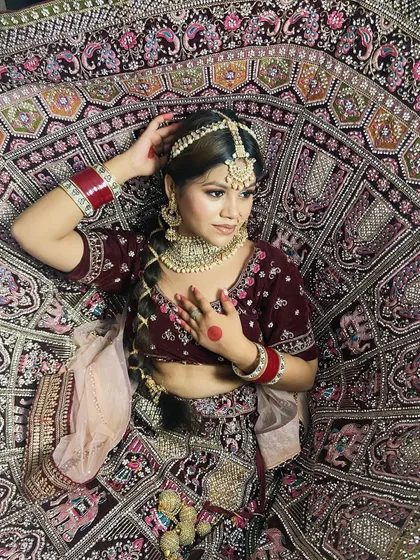 An artistic top-down shot of a bride in a deep maroon velvet lehenga. Our students learn to think about the entire presentation, including how the makeup works with intricate outfits.