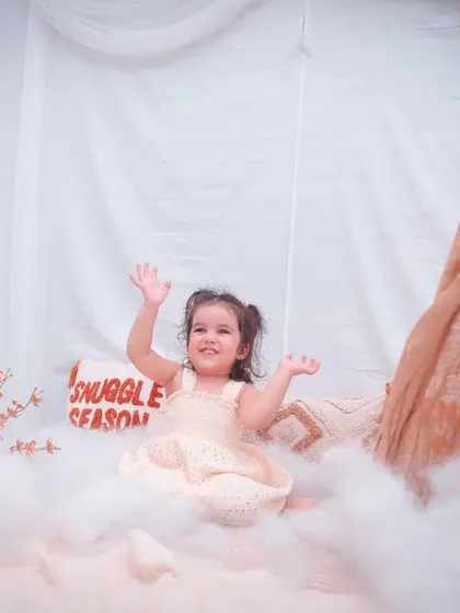 A happy girl with her arms up, playing in a boho-themed teepee setup. We create a fun environment to bring out natural expressions.