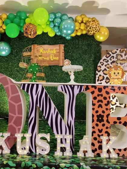 A full stage setup for a jungle-themed first birthday. This decor features large 'ONE' letters with animal prints, a green wall backdrop, and character cutouts.
