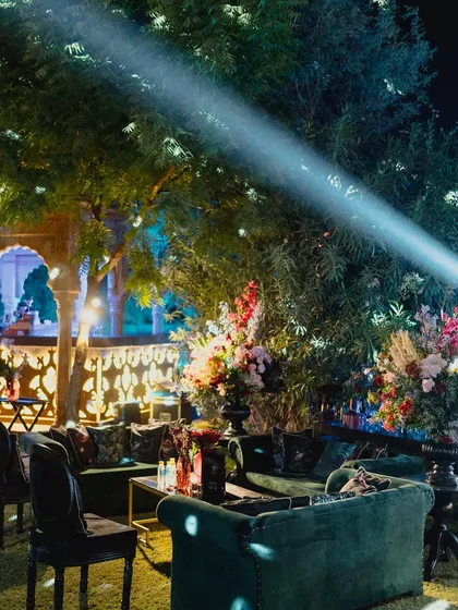 A cozy lounge area under the trees, with spotlights creating a dramatic play of light and shadow on the plush green velvet sofas.