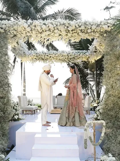 A breathtaking beachside wedding in Goa, with a mandap constructed entirely of baby's breath and white florals, creating a cloud-like effect against the sea.