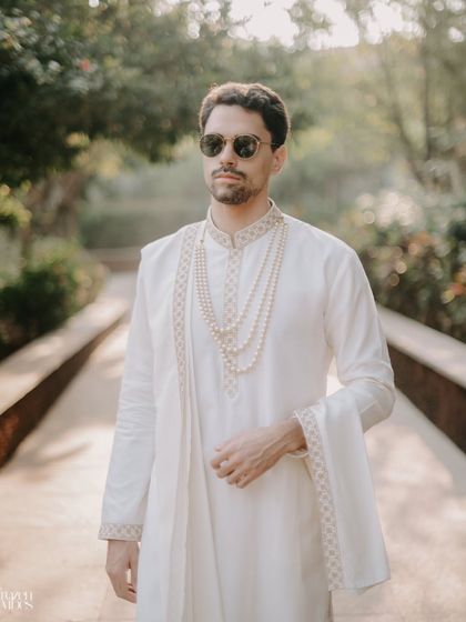 A stylish portrait of the groom in his elegant white wedding attire. The soft, natural light highlights the subtle details of his outfit.