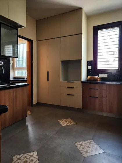 A modern kitchen featuring a mix of materials, including wood-finish and beige laminate cabinets, a black granite countertop, and patterned floor tiles. The design balances functionality with aesthetic details.