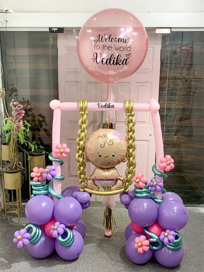 Welcoming Baby Vedika with this unique and intricate sculpture. A tiny baby balloon sits on a swing adorned with flowers, all held up by balloon columns, creating a truly special and handcrafted welcome gift.