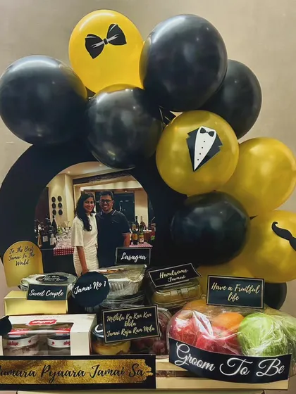 Welcome the 'Jamai Raja' into the family with a hamper fit for a king. This groom-to-be gift is filled with his favorite foods like lasagna, fresh fruits, and snacks, all presented with a fun and stylish black and gold theme.