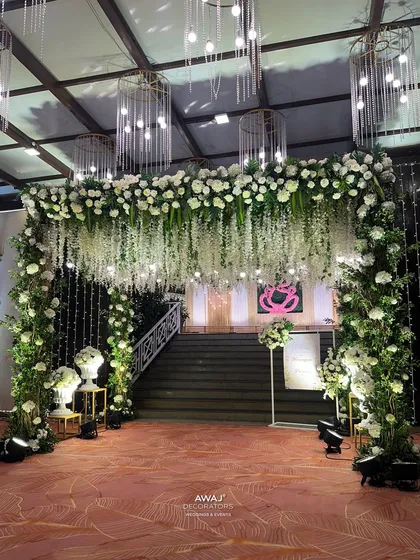 The grand entrance archway, covered in white flowers and greenery, with a hanging canopy of wisteria and modern chandeliers.