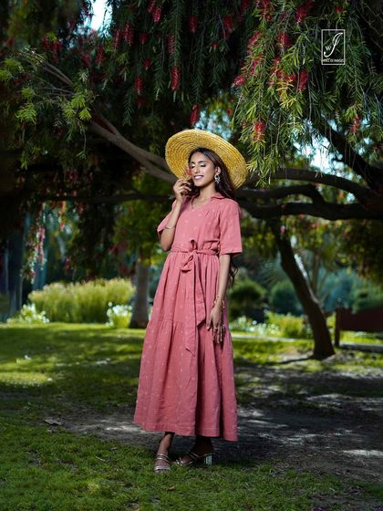 A standing portrait under a flowering tree, with the model's straw hat adding to the charming, rustic aesthetic of the outdoor shoot.